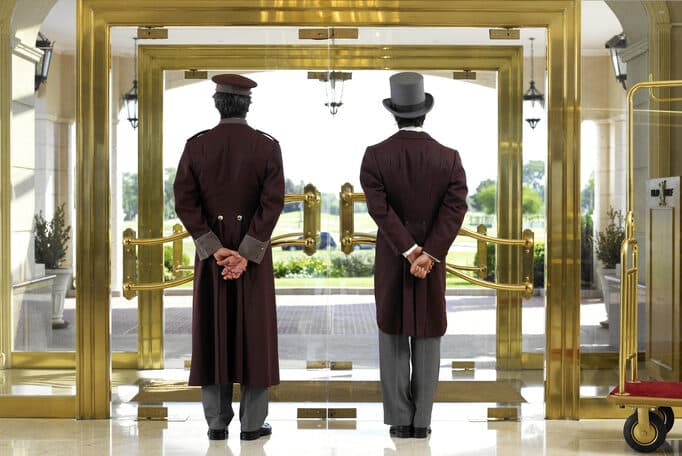 Concierge and bellboy standing at hotel entrance, rear view
