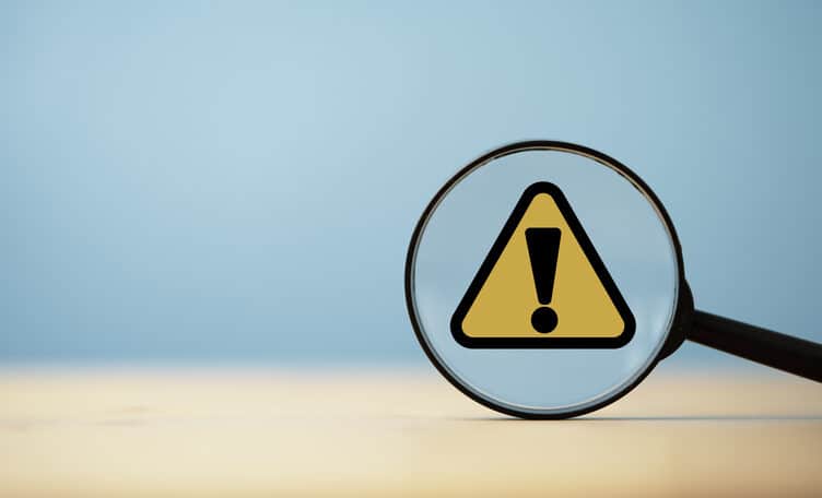 Yellow triangle caution warning sign inside of magnifier glass on blue background